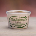 A 6 oz plastic tub of Mom Blakeman's Original Creamed Pull Candy, featuring a white container with a clear lid and green decorative text, set against a soft pink background.