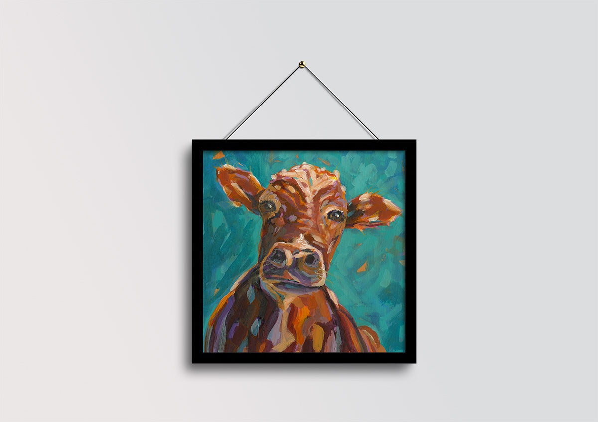 A framed painting of a brown cow on a teal background, hanging from a black wire against a light gray wall.