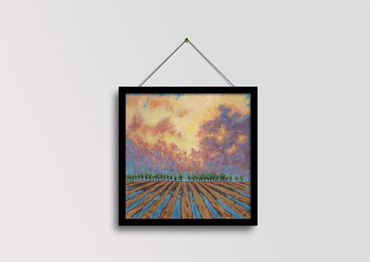 A framed landscape painting of a field under a dramatic sunset sky, hanging from a black string against a light gray wall.