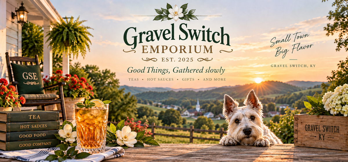 A promotional banner for Gravel Switch Emporium featuring a small white dog sitting on a wooden fence in a scenic rural landscape at sunset. The scene includes a porch with a chair, flowers, a glass of iced tea, and a wooden crate labeled 'Gravel Switch Emporium KY'.