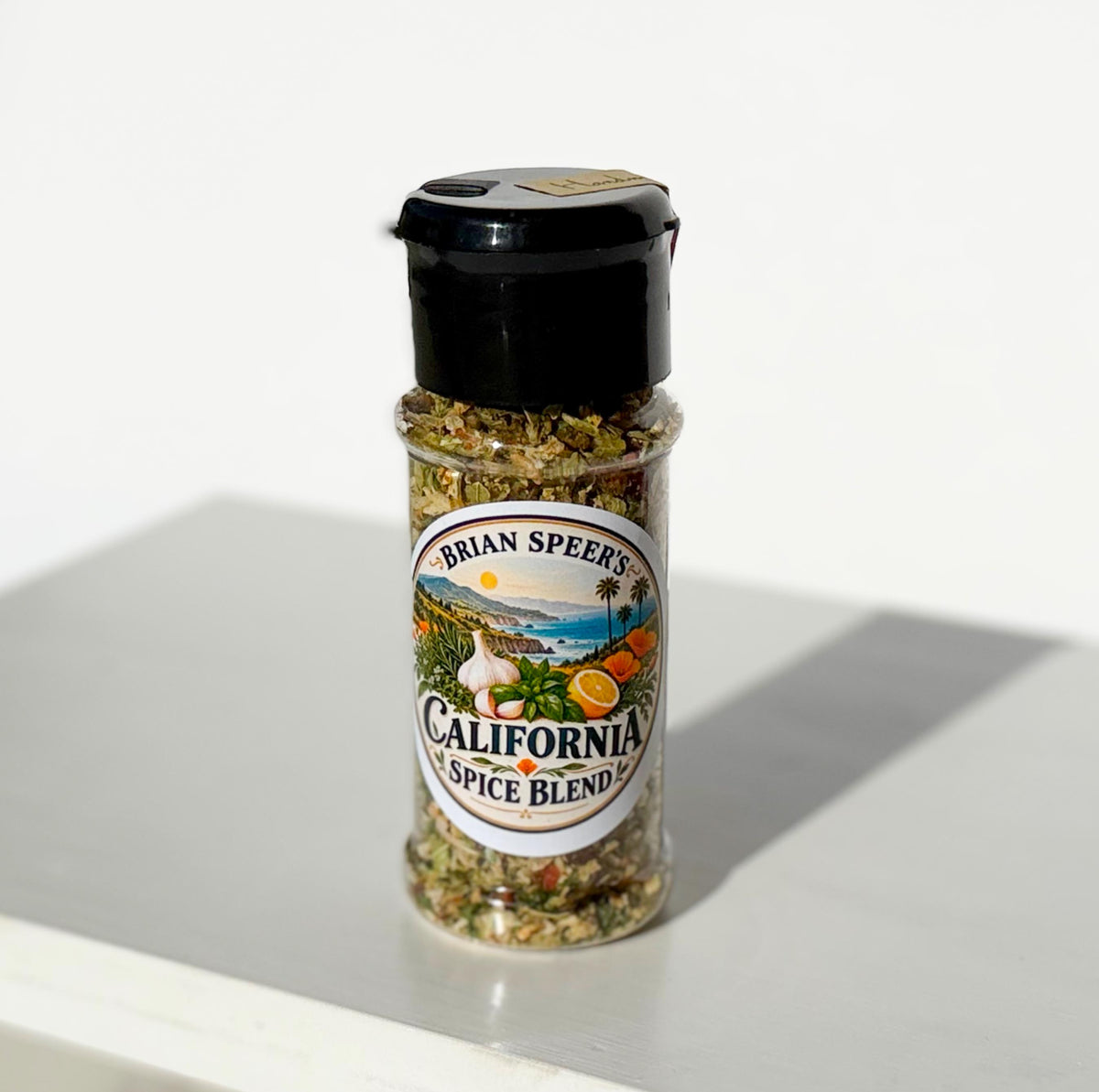 A bottle of Brian Speers California Spice Blend seasoning with a black shaker cap and a colorful label, set on a white surface with a soft shadow.