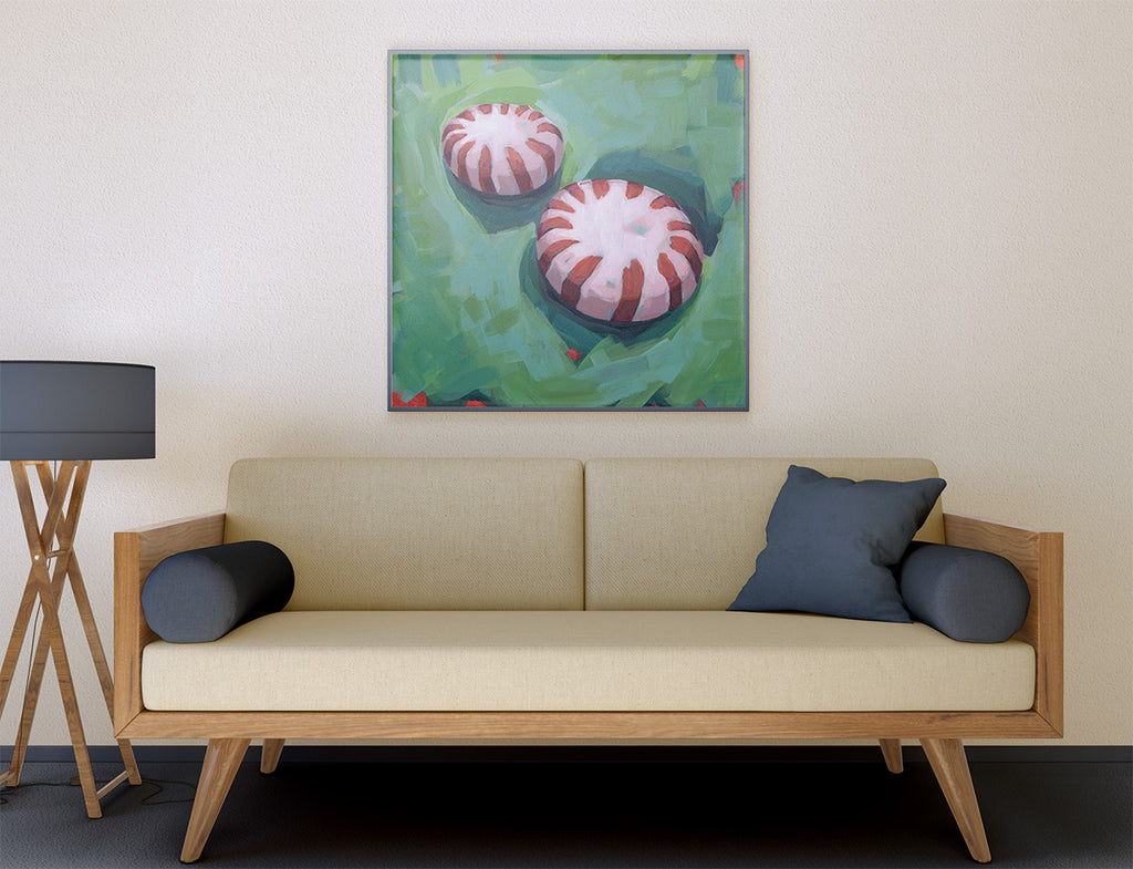 A framed square wall art print depicting two red-and-white striped round motifs on a green textured background, displayed above a beige sofa in a modern living room setting.