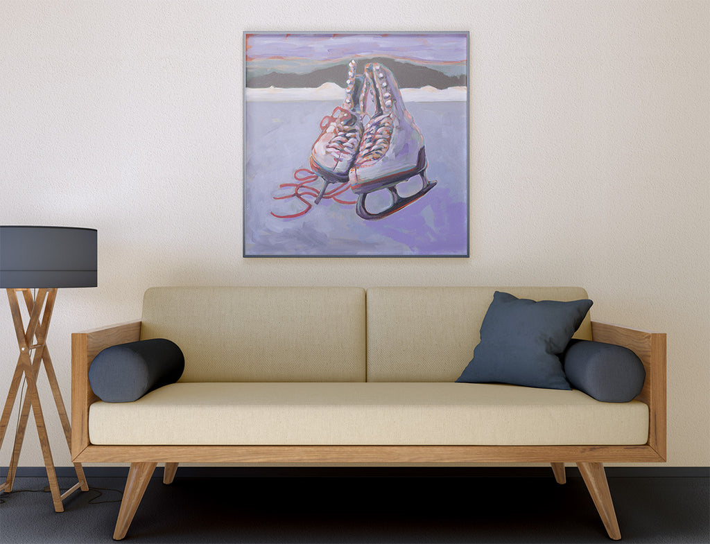 A framed painting of a pair of ice skates hanging on a beige wall above a mid-century modern sofa with dark blue pillows. A black floor lamp is visible on the left.
