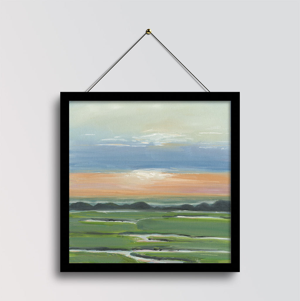 A framed landscape painting hanging on a light gray wall. The artwork depicts green fields and distant dark hills beneath a blue sky with a warm orange band near the horizon.