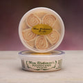 Two round plastic tubs of Mom Blakeman's Potato Candy stacked on a light surface against a dark purple gradient background. The top tub is open, showing spiral potato candy rolls inside, with a gold oval label.